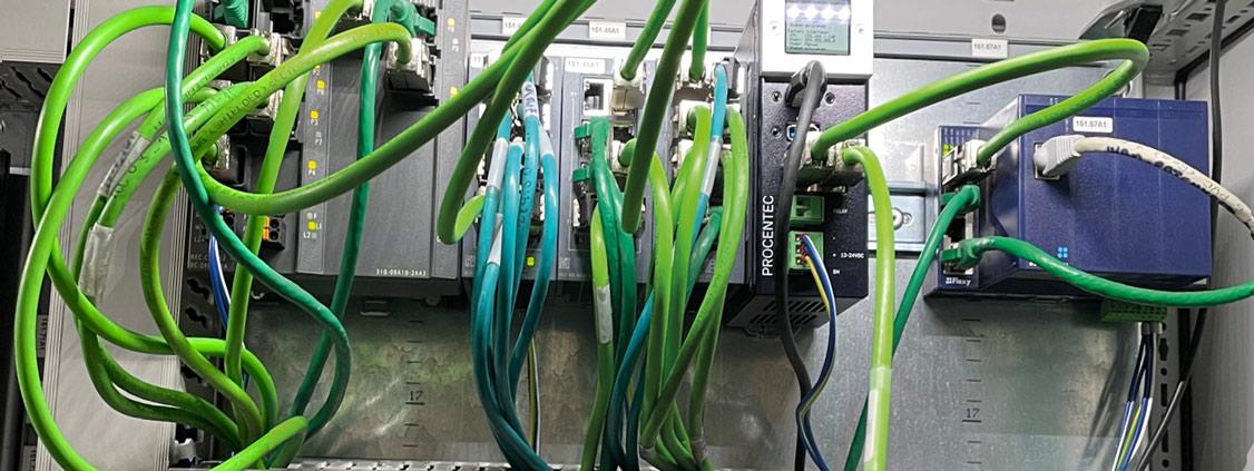 Industrial network equipment inside an electrical cabinet with multiple green communication cables.